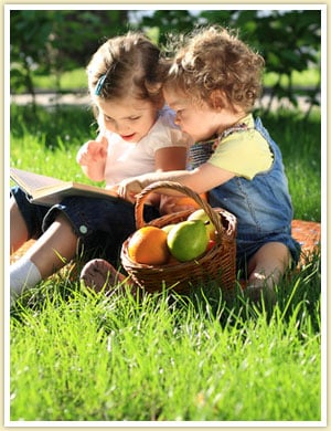 two little girls sitting on the grass reading a book