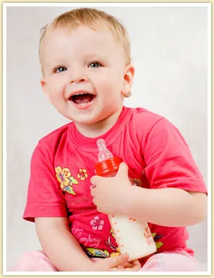 cute toddler holding a bottle of milk while smiling