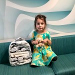 little girl sitting on blue couch with grey backpack