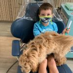 Child patient with a mask and the emotional support dog on him