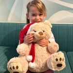 Girl hugging large teddy bear with red scarf in clinic